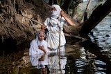 A Mandaean women dressed in traditional clothing  is baptised by a priest in the Nepean river in Penrith.