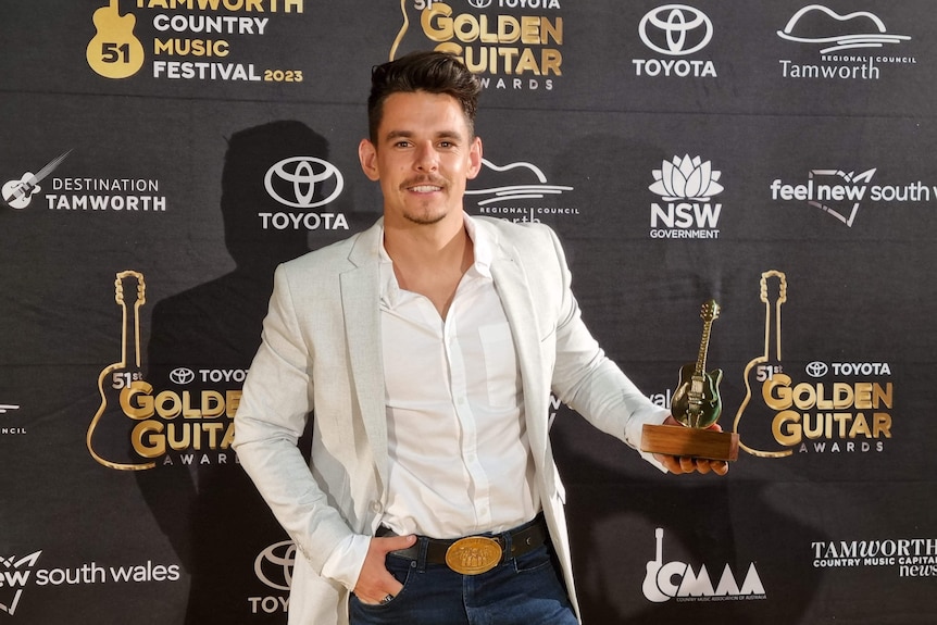 A smiling James Johnston holding a Golden Guitar Award