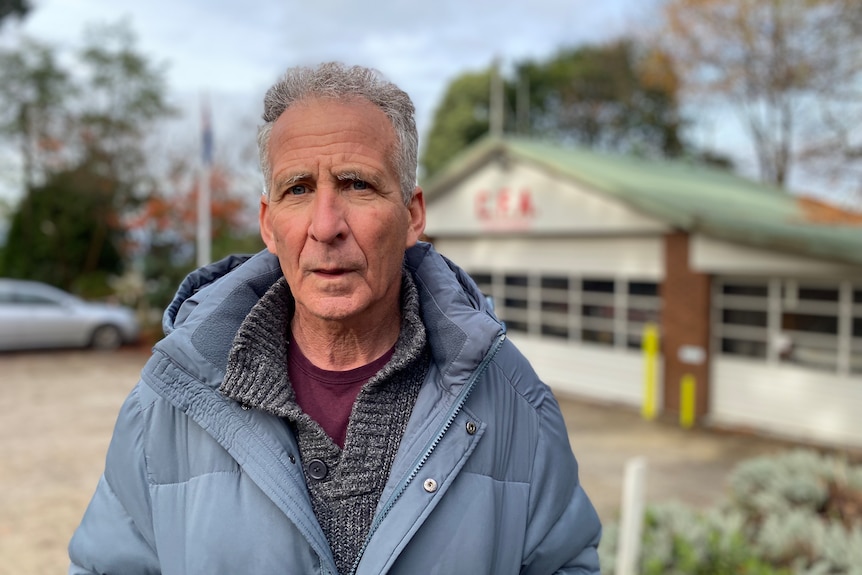 Bill Robinson, dressed in a warm jacket, appears serious as he stands outside a CFA-branded building.