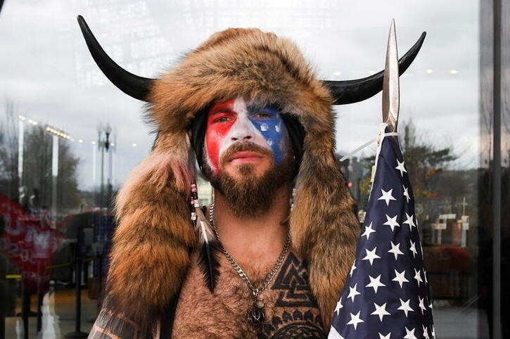 Jacob Chansley looks into the camera as he wears horns and a fur hat with face paint on.