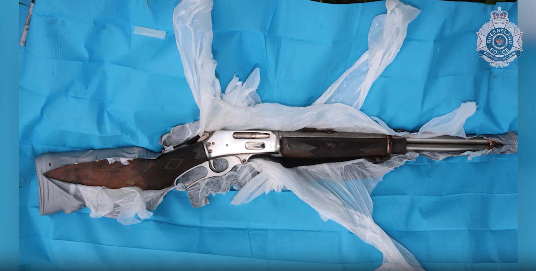 Un rifle semiautomático tirado entre plásticos triturados. Esta imagen presenta una marca de agua de la policía de Queensland.