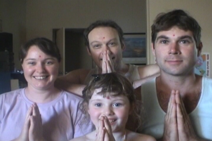 Two men, a woman, and a child hold their hands in prayer