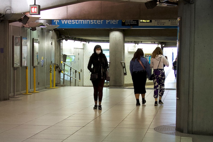 A woman wearing a mask walks in London's tube station.