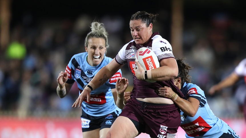 A women's rugby league player charges through defenders 