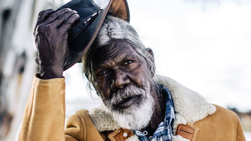 Actor David Gulpilil, an older Yolngu man in shearling coat taking off his akubra, in the documentary My Name is Gulpilil