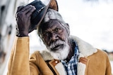 Actor David Gulpilil, an older Yolngu man in shearling coat taking off his akubra, in the documentary My Name is Gulpilil