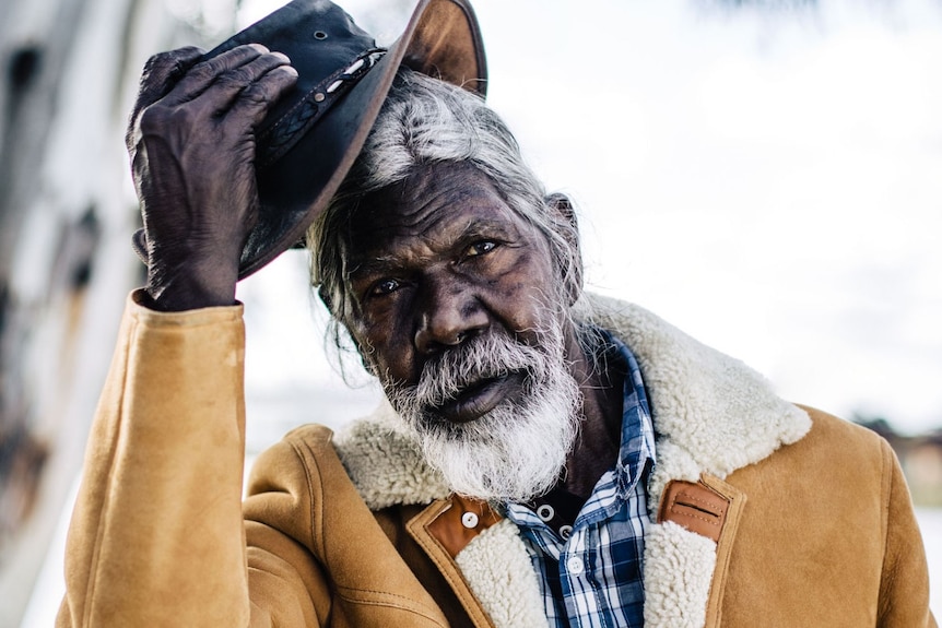 Actor David Gulpilil, an older Yolngu man in shearling coat taking off his akubra, in the documentary My Name is Gulpilil