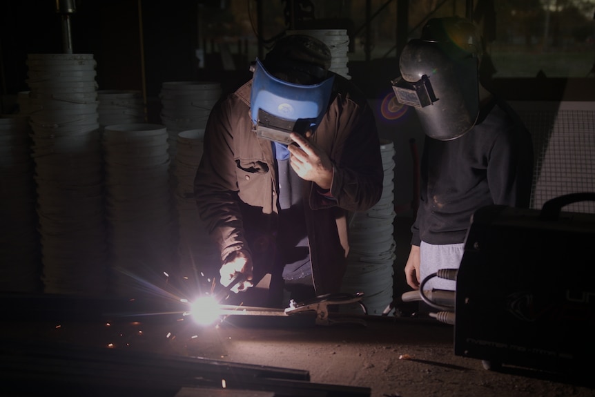 Two people wearing protective gear using a soldering iron