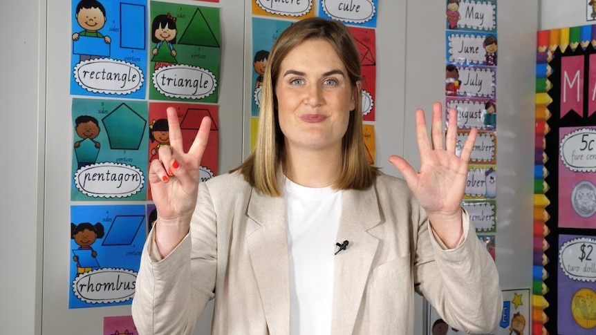 Female teacher in classroom holds up 7 fingers