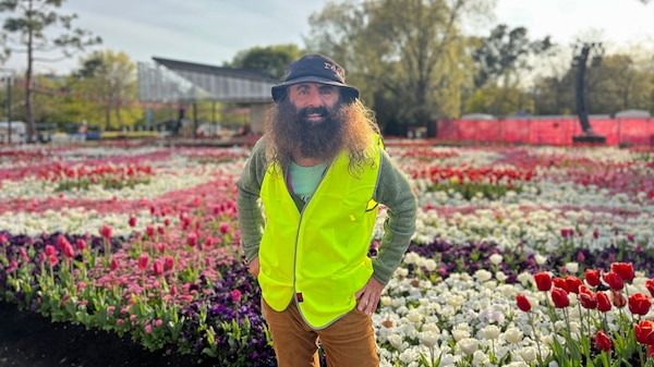 Costa wearing a high-viz vest, standing in front of a floral garden display.