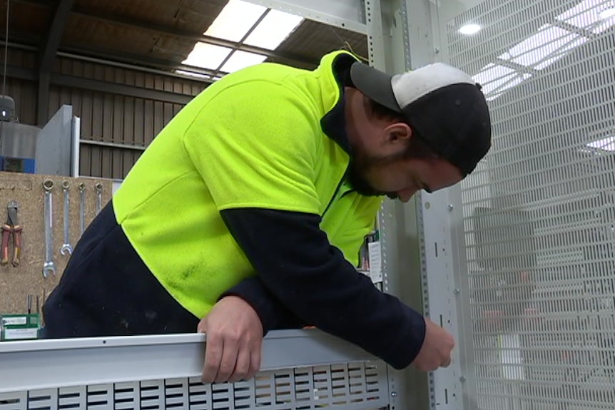 A man wearing a backwards cap and a hi-vis jumper marking something on a metal structure.