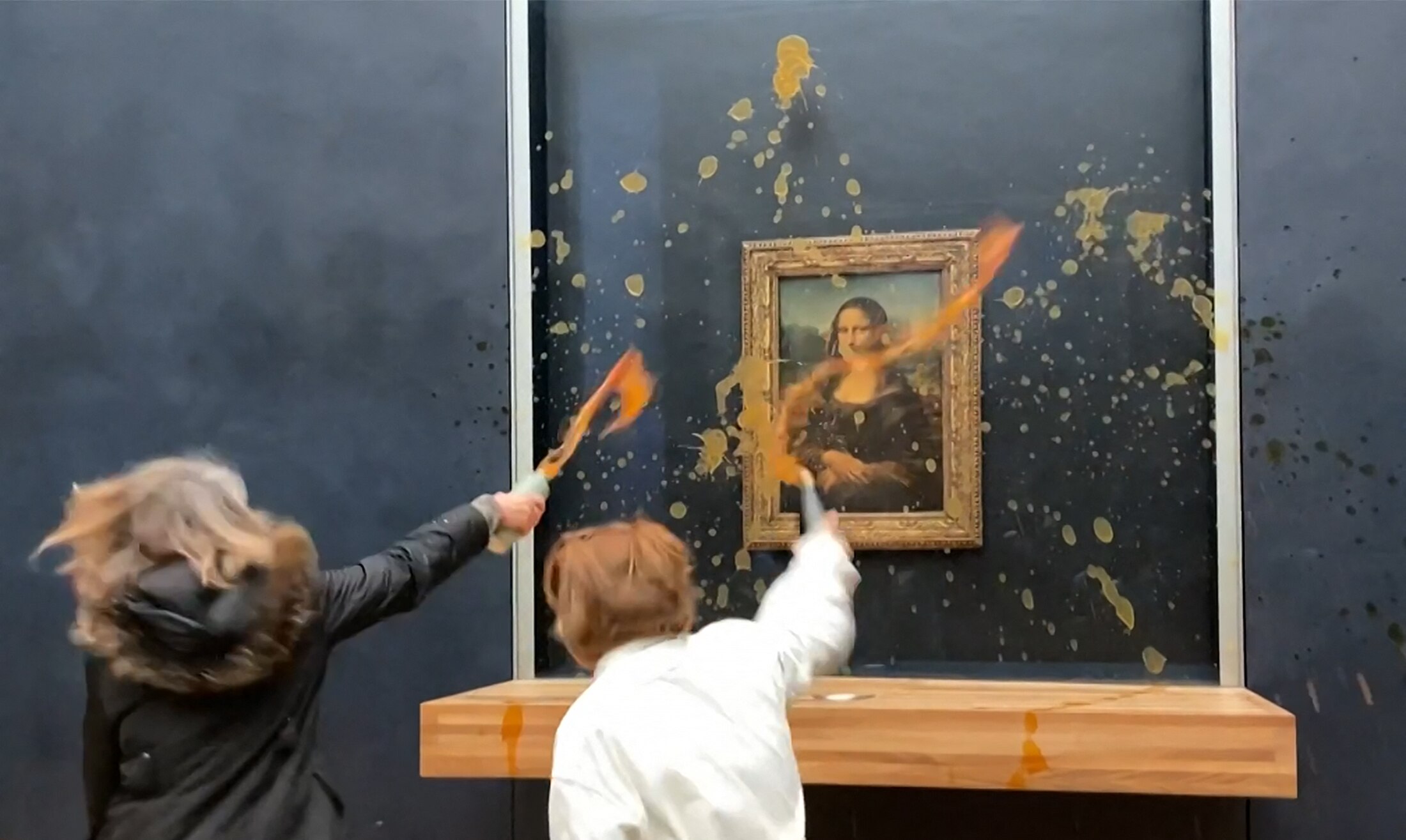 Two people throw soup towards a painting.