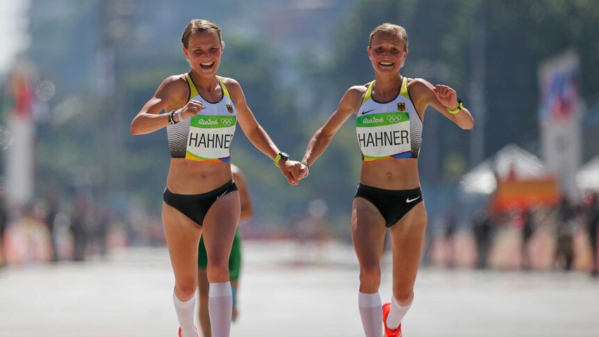 Lisa Hahner and Anna Hahner hold hands and smile as they cross the finish line