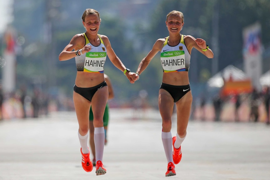 Lisa Hahner and Anna Hahner hold hands and smile as they cross the finish line