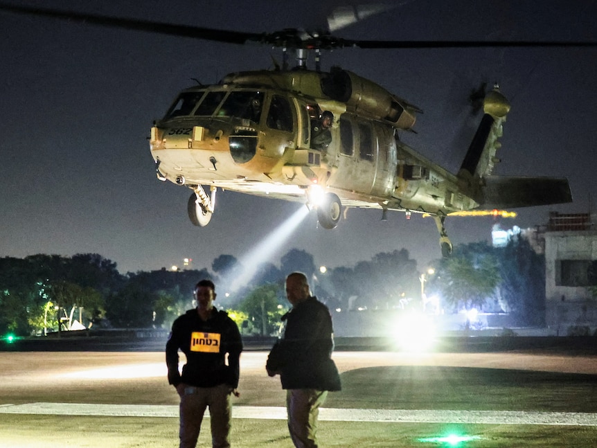 Two men standing in front of a helicopter at night. 