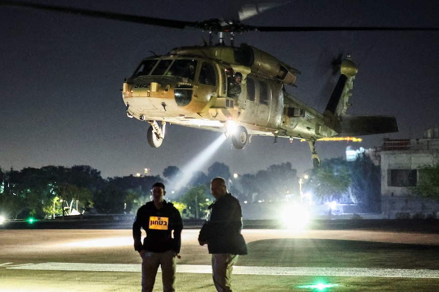 Two men standing in front of a helicopter at night. 