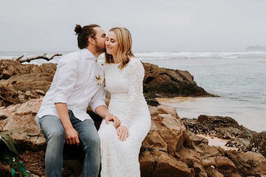 Liz Marie and her husband kiss on a log on their wedding day.