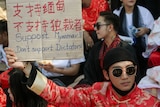 A man in a red traditional Chinese outfit holds up a sign at a protests that reads 'Support Myanmar, don't support Dictators'.