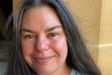 A portrait of a Indigenous Australian woman with long brown hair standing in front of artwork