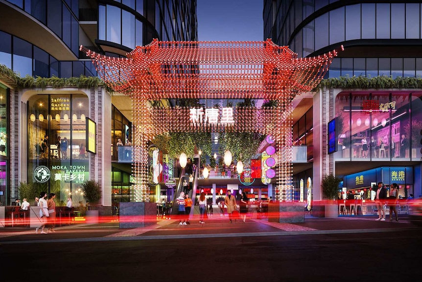 A picture showing a Chinese-style gate made of red lights as people cross roads between high sky rise buildings