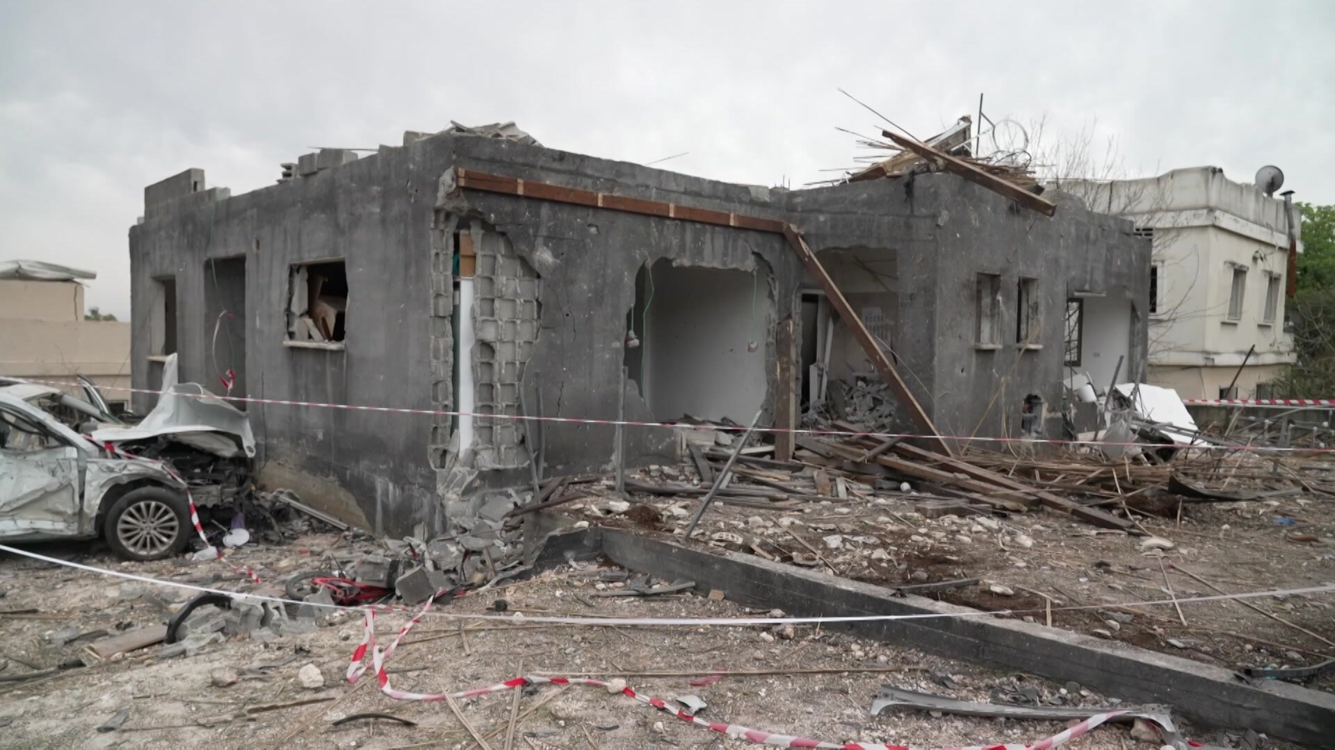 A heabily damaged structure with a destroyed vehicle alongside.