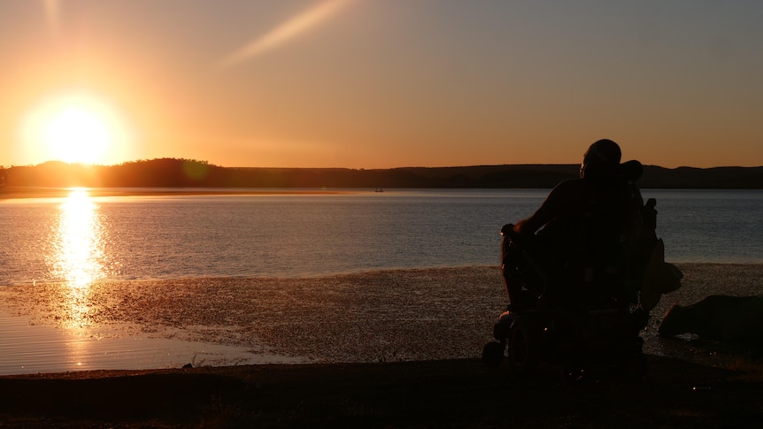 Man in wheelchair watches sunset over lake