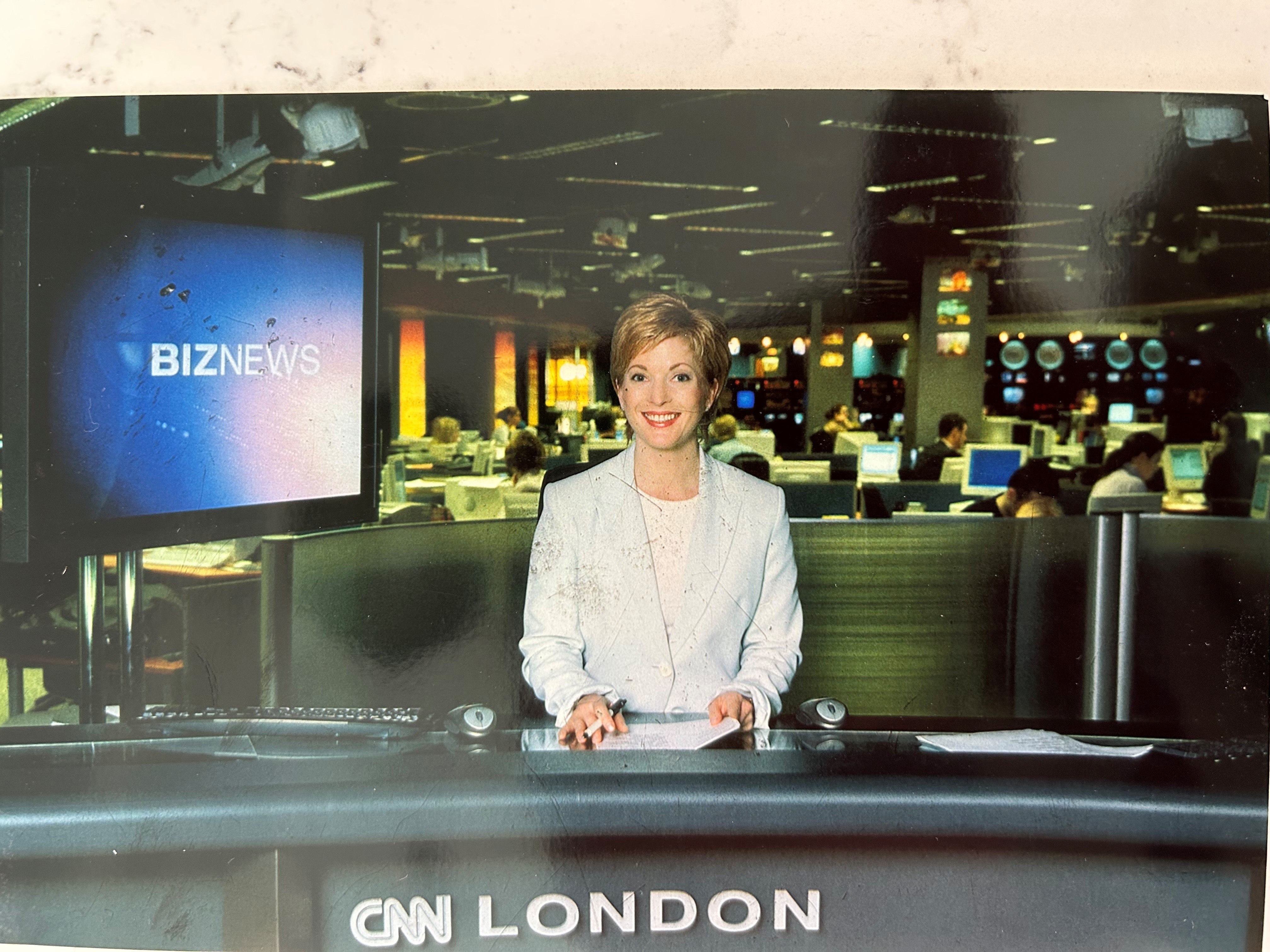 A photograph of a woman behind desk and a screen reading biznews behind her