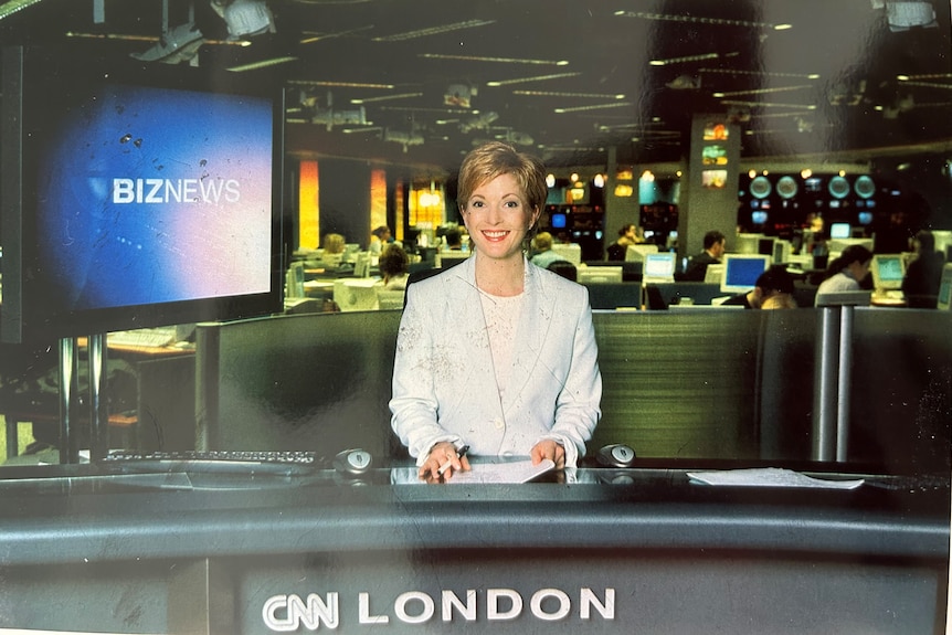 A photograph of a woman behind desk and a screen reading biznews behind her