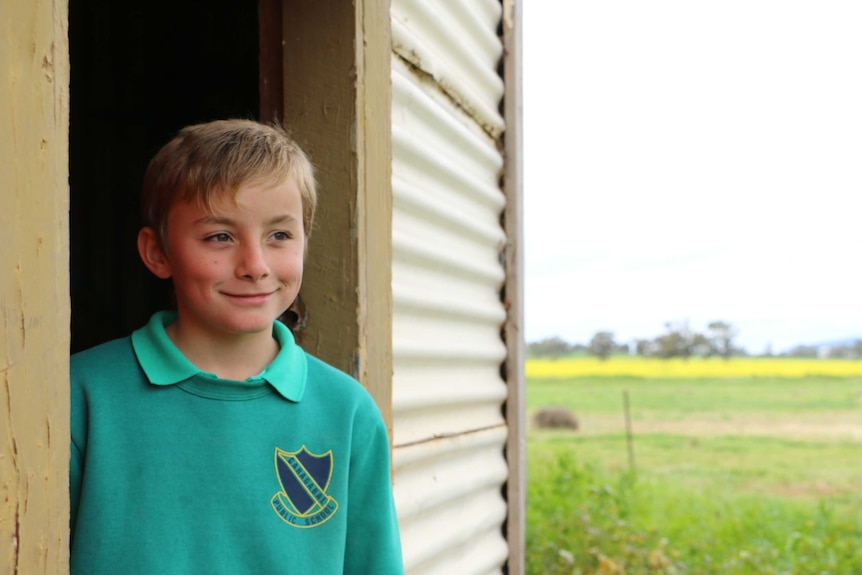 A smiling boy in a doorway with a green paddock and canola growing in the background