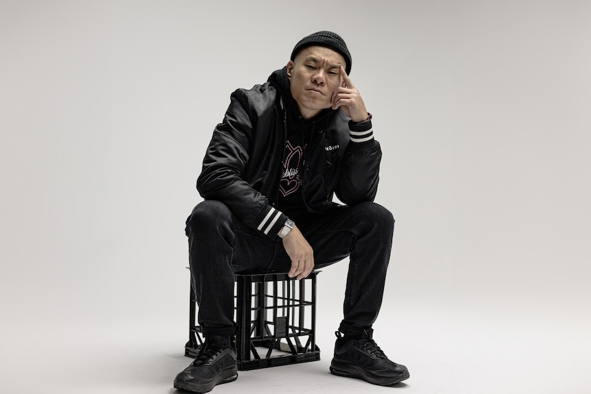 An asian man sits on a milk crate