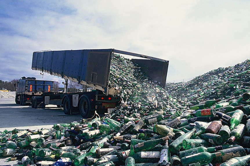 A dump truck tipping out glass bottles for recycling