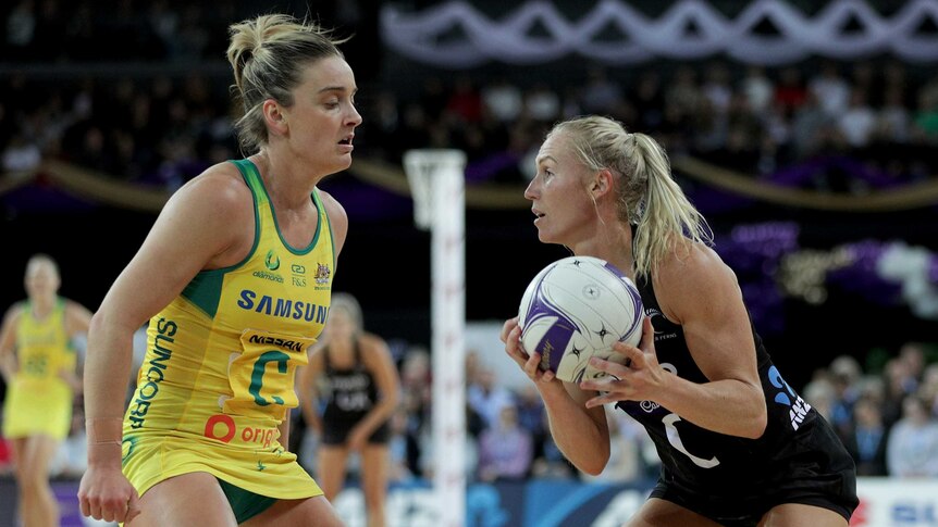 An Australian netballer stands in front of an New Zealand opponent holding the ball in the Constellation Cup Test.