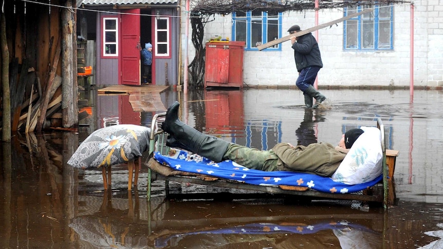 A man rests on a bed in floodwaters.