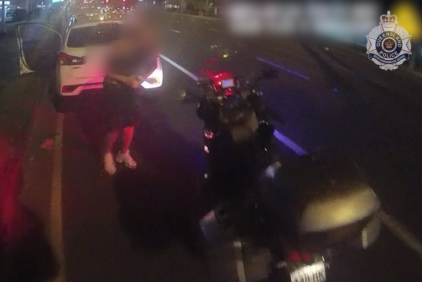 A man standing behind a while car and in front of a police motor cycle