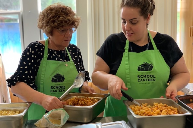 Two women preparing food in a school canteen.