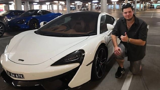 A man kneels next to a white, luxury car giving the thumbs up