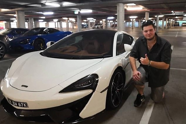 A man kneels next to a white, luxury car giving the thumbs up
