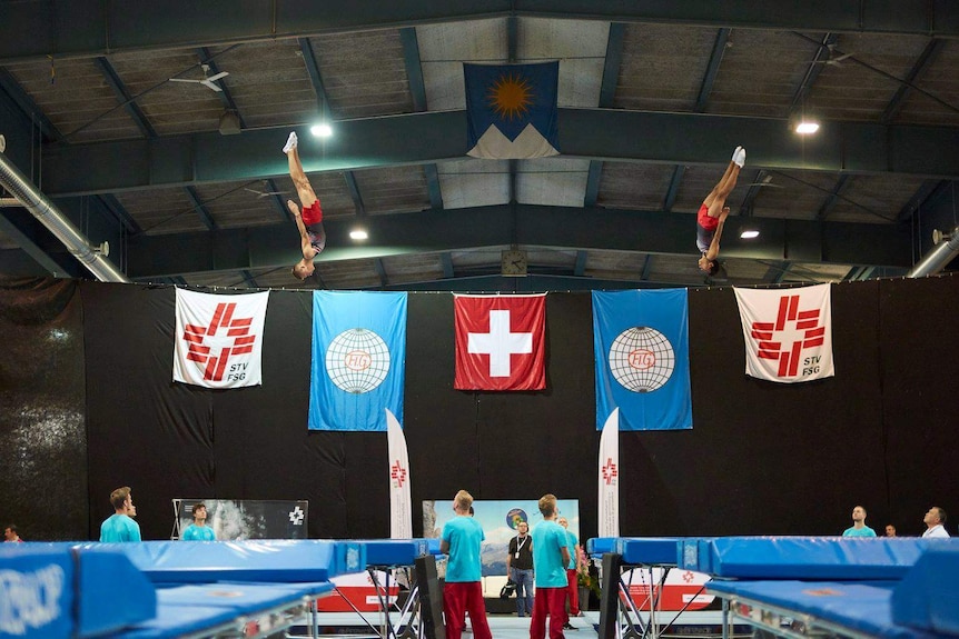 Two men in the air above two trampolines during a competition.