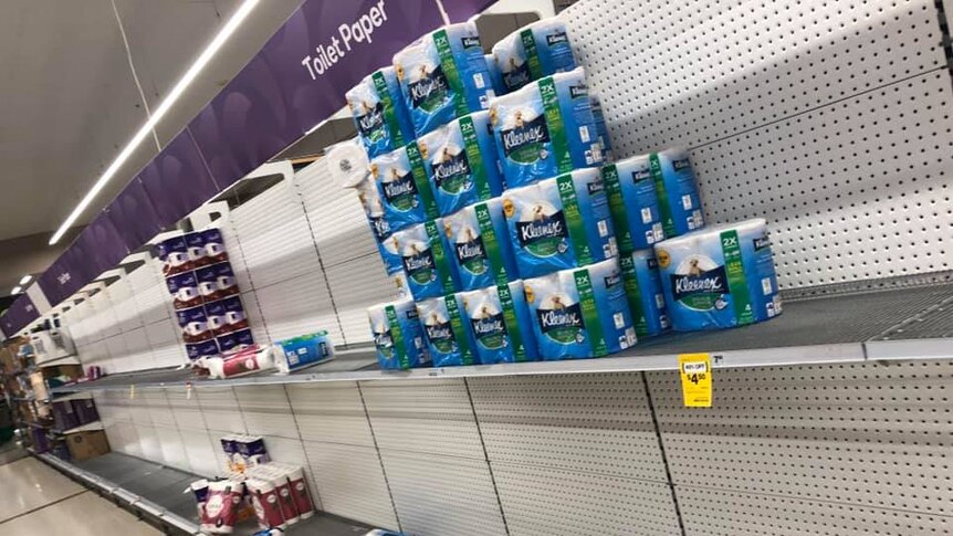 An aisle in Woolworths supermarket with mostly empty shelves labelled Toilet Paper