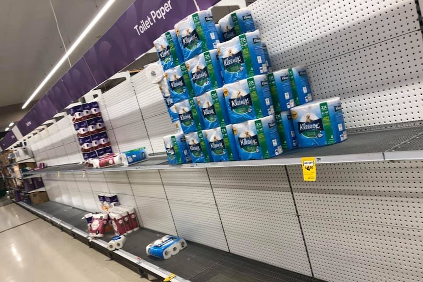 An aisle in Woolworths supermarket with mostly empty shelves labelled Toilet Paper