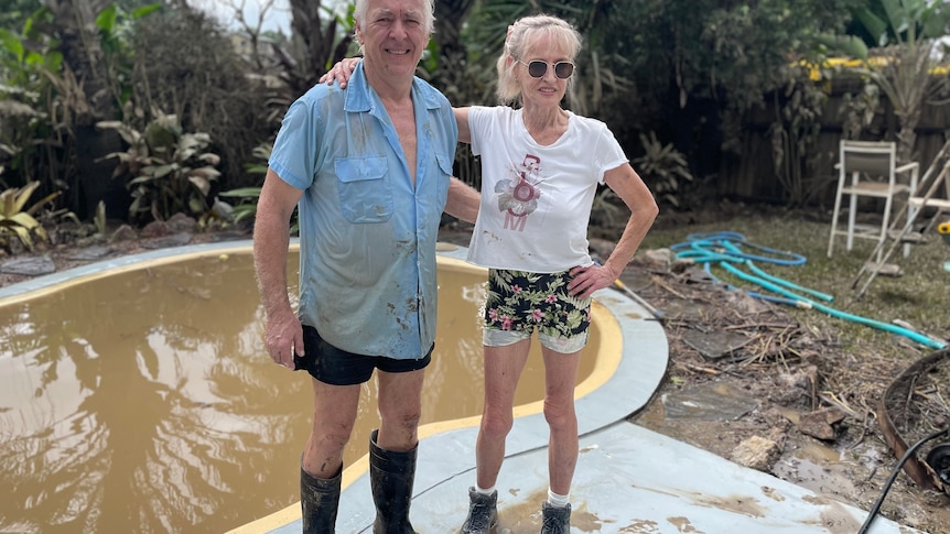 Woman and man standing in front of swimming pool filled with brown water