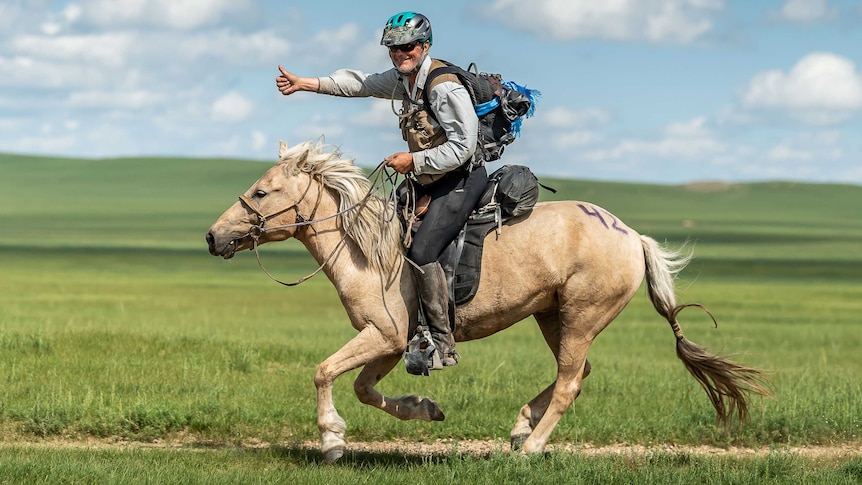 A man in his 70s rides along on a horse in an open field.