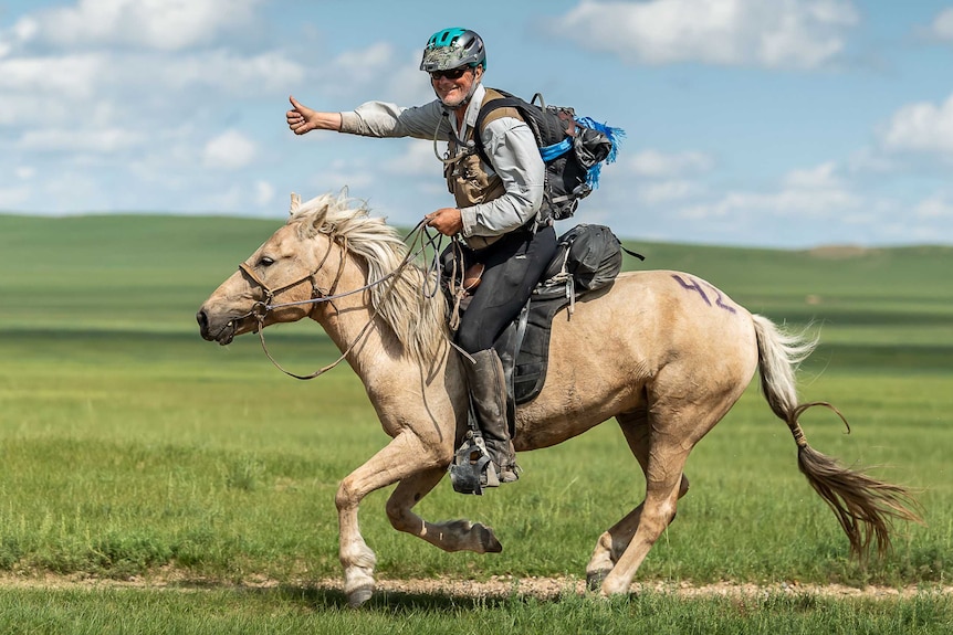 A man in his 70s rides along on a horse in an open field.