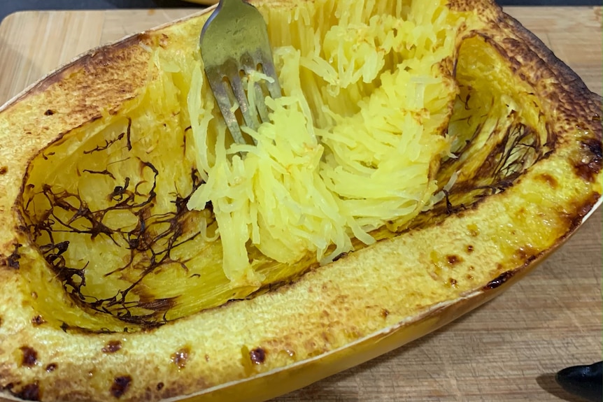 A cooked spaghetti squash is forked through and its fibrous insides look like angel hair pasta