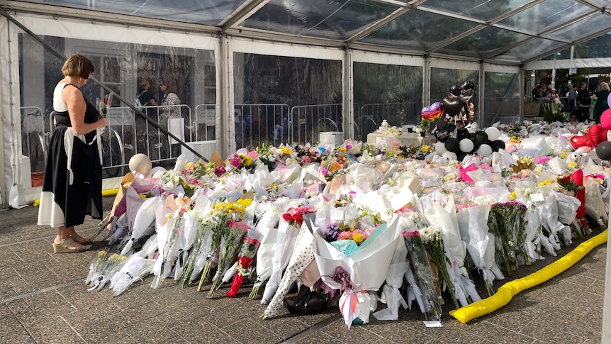 A woman standing next to a flower memorial.