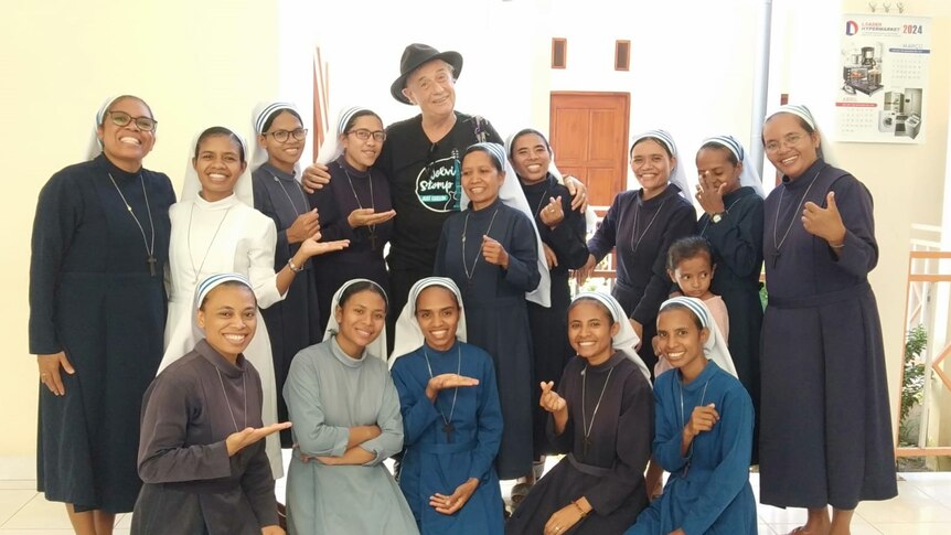 a man wearing a wide brimmed hat standing among a group of nuns wearing habits