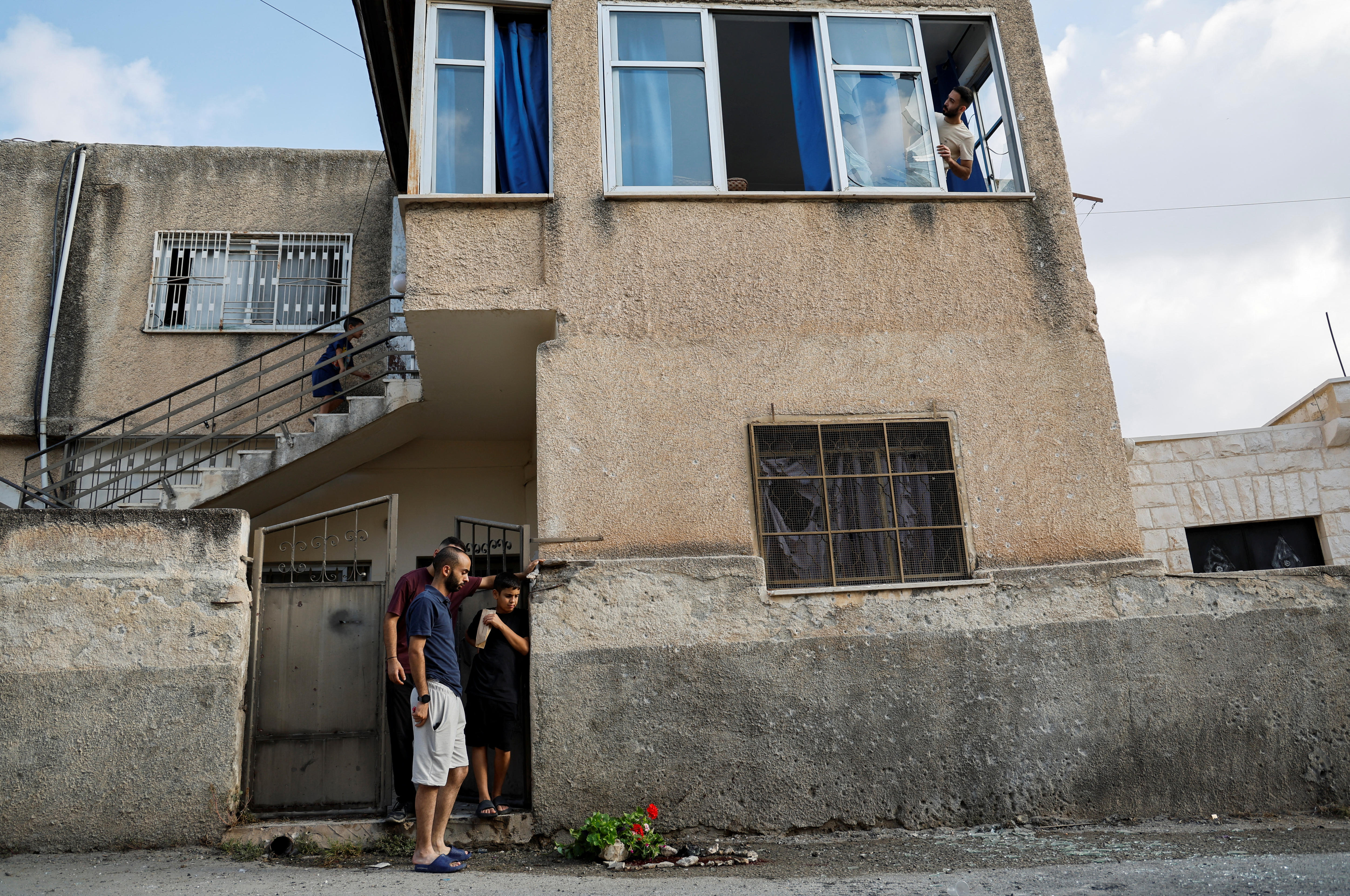 A Palestinian man looks out of a broken window while others look at a streak of blood on the ground below.