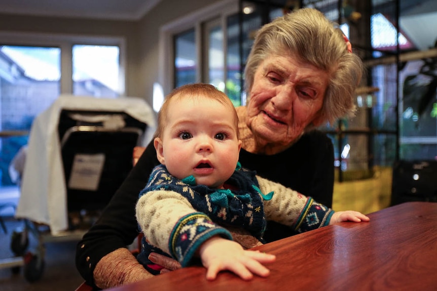 Six-month-old Lola Fletcher sits on table in front of Morleen Templeman