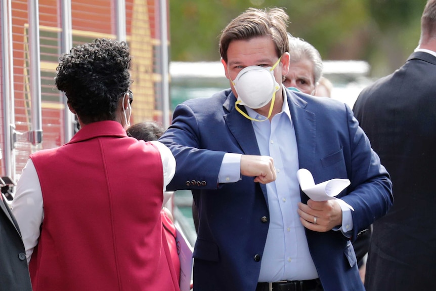 Ron DeSantis with a face mask on bumping elbows with a woman