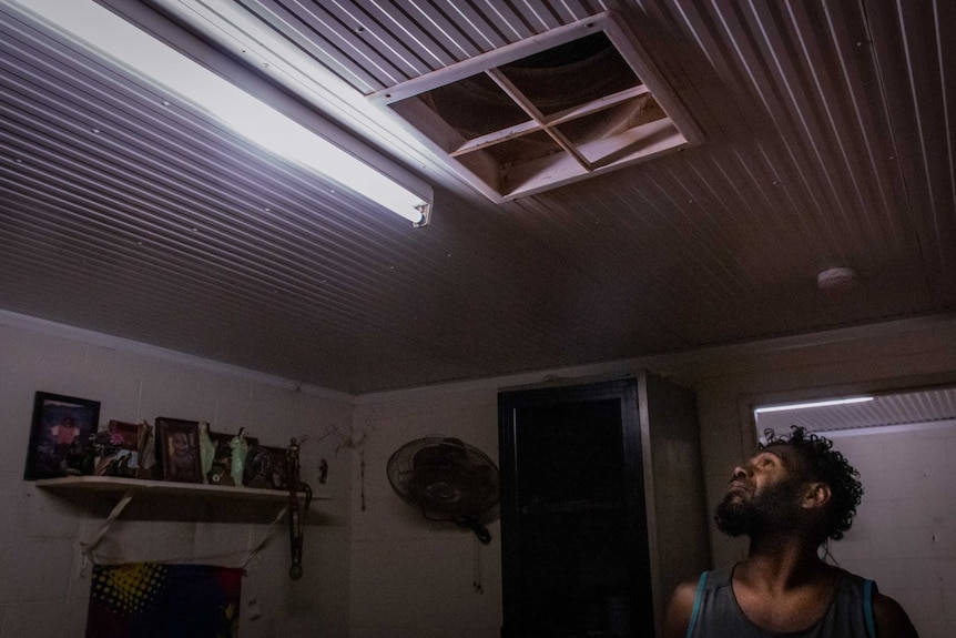 Indigenous man Charlie Lynch looks at a square light fitting on the ceiling.